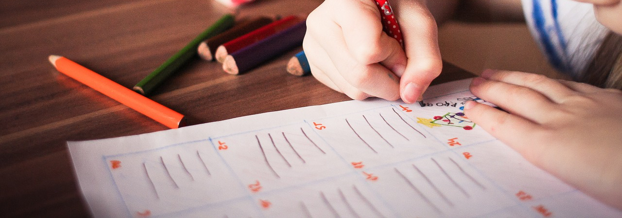 A young student practising handwriting with coloured pencils during an English lesson